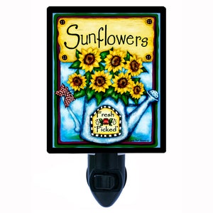 May include: A night light featuring a blue watering can with a bouquet of yellow sunflowers. The watering can has a yellow label that says "Fresh Picked". The background is a blue sky with white clouds. The sign above the watering can says "Sunflowers".