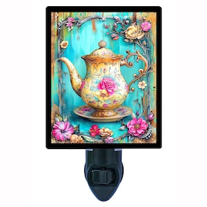 May include: A decorative night light featuring a vintage teapot design. The teapot is yellow with pink and blue floral accents, set against a turquoise background. The design is framed with floral embellishments and a black border.