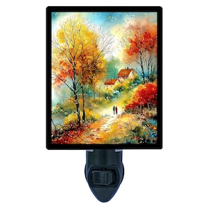 May include: A night light featuring a watercolor painting of an autumn landscape. The artwork depicts a path leading to houses, with trees in shades of yellow, orange, and red. The night light has a black border and a black base with an on/off switch.