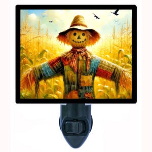 May include: A night light featuring a colorful painting of a scarecrow in a cornfield. The scarecrow has a straw hat and a stitched smile. The background shows a field of golden corn stalks under a blue sky with birds.