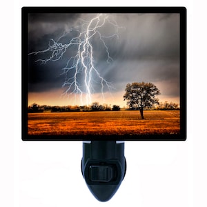 May include: A nightlight with a picture of a lightning storm over a field with a lone tree in the middle.
