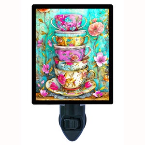 May include: A stack of four colorful teacups with floral patterns, on a white saucer, with a floral background. The teacups are stacked on top of each other, with the largest cup on the bottom and the smallest cup on top. The teacups are decorated with pink, blue, yellow, and green flowers. The background is a turquoise blue with a floral pattern.