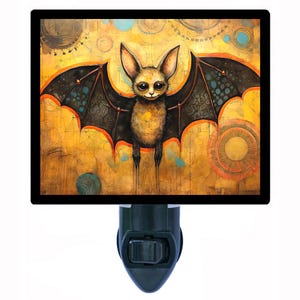 May include: A nightlight featuring a whimsical illustration of a bat with large, black wings against a yellow, orange, and brown background with circular patterns.