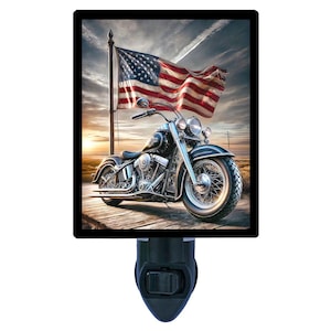 May include: A black motorcycle with a chrome exhaust and a large American flag waving in the background. The motorcycle is parked on a paved road with a sunset in the background.