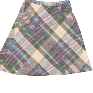 May include: A vintage plaid skirt in a classic A-line silhouette. The skirt features a colorful plaid pattern with shades of purple, green, blue, and cream. The fabric appears to be a woven material, and the skirt has a waistband.