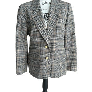 May include: A plaid blazer in black, tan, and white, displayed on a black mannequin. The blazer has two gold buttons and two front pockets. The fabric has a classic check pattern.