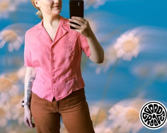 Puede incluir: Una camisa rosa de manga corta con cuello y dos bolsillos pequeños. La camisa se combina con pantalones marrones. El fondo es un cielo azul con flores blancas y un logotipo de "GOOD GROOVE".