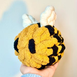 May include: A handmade plush bee toy with a yellow and black body and white wings. The bee is made of a soft, textured material. The toy is designed to resemble a bumblebee.