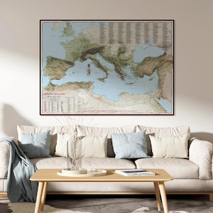 May include: A framed vintage map of Europe and the Mediterranean, with detailed geographical features and text. The map is in shades of blue, green, and tan, and is displayed above a beige sofa with blue and patterned pillows.