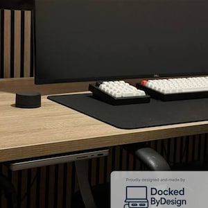 May include: A desk setup featuring a black monitor, two white and black keyboards, and a black mouse. The text "SlideUnderV1" and "UNDER-DESK DOCK FOR APPLE MACBOOK PRO 14" is visible. A laptop is docked under the desk. The product is designed by Docked ByDesign.