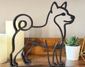 Minimalist Shiba Inu line art sculpture in matte black on a wooden shelf with candles and succulents, modern Japanese dog decor for home or office.