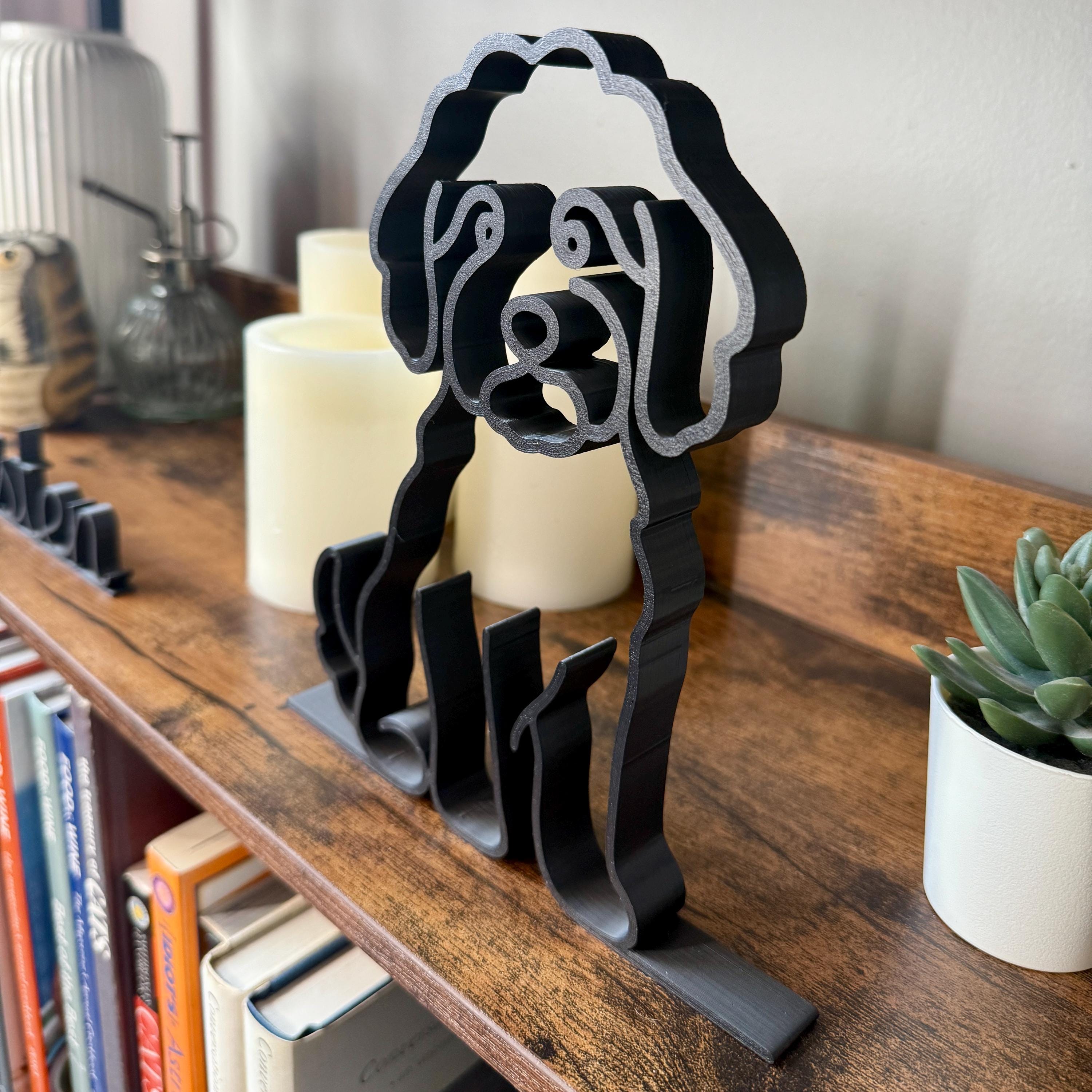 Matte black Mini Goldendoodle line art sculpture on wooden shelf with books and candle