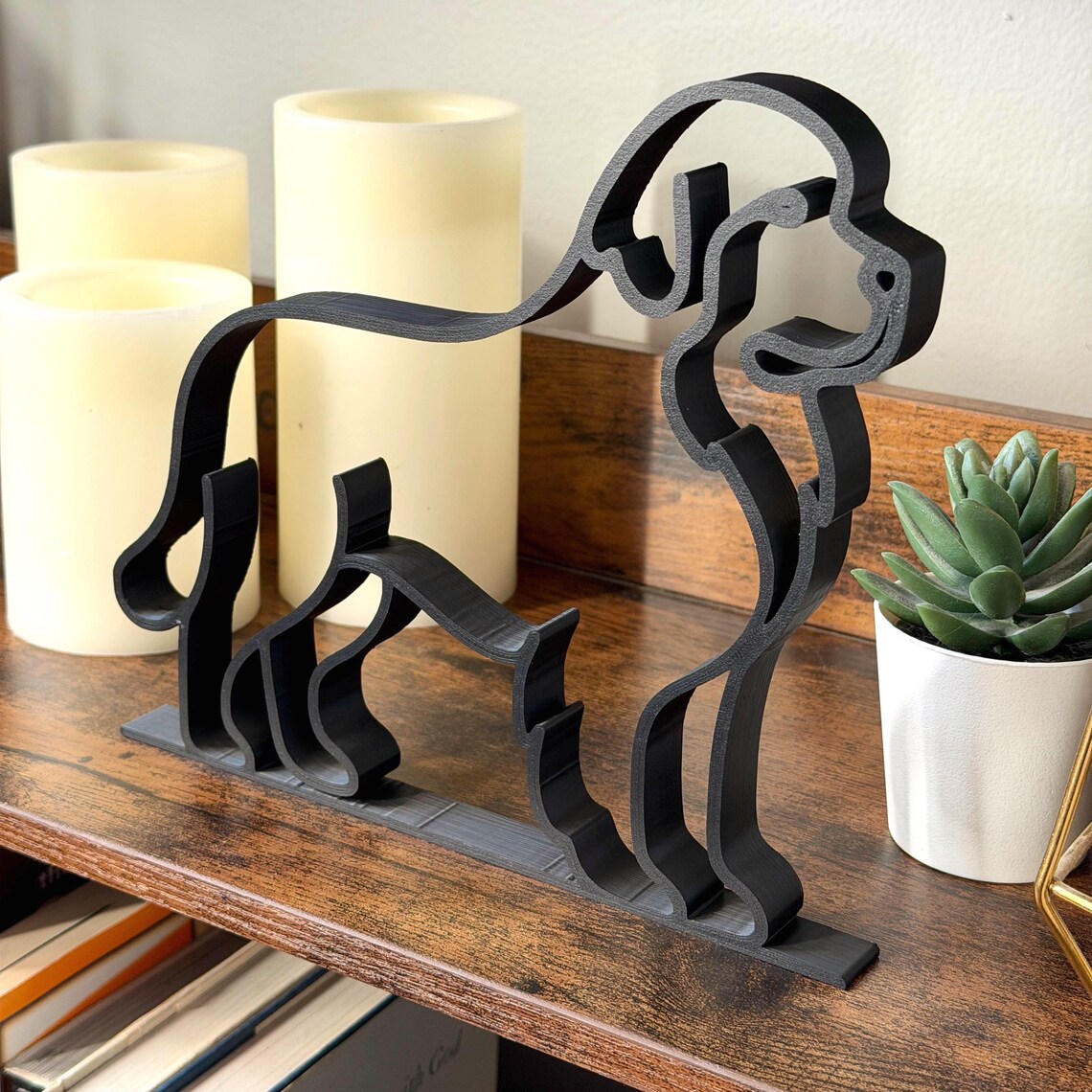 Side angle view of a Newfoundland Dog line art sculpture in matte black finish, styled on a shelf with candles and greenery. This modern minimalist decor piece is 3D printed for crisp detail and smooth edges. Perfect gift for dog lovers, Newfoundland enthusiasts, or pet parents who appreciate contemporary design. Lightweight, durable, and handmade with care, it blends effortlessly into modern, Scandinavian, or eclectic home interiors.