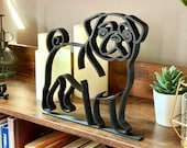 Minimalist pug line art sculpture in matte black shown on a wooden bookshelf with candles, books, and plants. This modern dog shelf sitter decor captures the pug’s playful face, curly tail, and sturdy stance. Perfect as bookshelf decor, reading nook art, or a gift for pug lovers. Lightweight 3D printed sculpture blends with modern, Scandinavian, and eclectic home styles. Ideal office decor or pet lover gift.