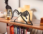 Modern 3D printed pinky promise sculpture made from black minimalist line art, displayed on a wooden shelf. This handmade line art decor features two hands linked in a pinky swear, symbolizing trust, loyalty, and love. Ideal as a friendship gift, romantic anniversary decoration, or stylish addition to modern and boho home decor. Surrounded by white candles and gold accents, the sculpture creates a warm, aesthetic vibe.