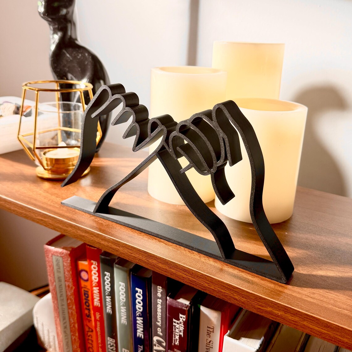 Modern 3D printed pinky promise sculpture made from black minimalist line art, displayed on a wooden shelf. This handmade line art decor features two hands linked in a pinky swear, symbolizing trust, loyalty, and love. Ideal as a friendship gift, romantic anniversary decoration, or stylish addition to modern and boho home decor. Surrounded by white candles and gold accents, the sculpture creates a warm, aesthetic vibe.