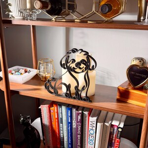 Styled lifestyle scene of a Maltipoo line art sculpture on a wooden display shelf with candles, glassware, vintage books, and decorative accents — modern minimalist Maltipoo home decor, doodle dog art, and a heartfelt Maltipoo gift idea for shelves, mantels, and dog lover homes.
