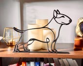 Close-up of a matte black bull terrier line art sculpture showing the breed's distinctive egg-shaped head, athletic body, and clean continuous-line silhouette, glowing candles backlighting the design — 3D printed minimalist dog decor and bull terrier gift idea for dog moms and dog dads.