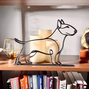 Close-up of a matte black bull terrier line art sculpture showing the breed's distinctive egg-shaped head, athletic body, and clean continuous-line silhouette, glowing candles backlighting the design — 3D printed minimalist dog decor and bull terrier gift idea for dog moms and dog dads.