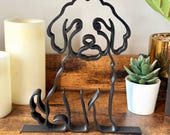 Minimalist Mini Goldendoodle sculpture on a wooden shelf styled with candles and a potted plant, showcasing its curly teddy-bear outline in matte black line art.