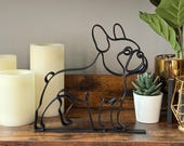 Minimalist French Bulldog sculpture in black matte finish, created in a sleek single line art style. Displayed on a shelf with greenery and candles, this modern Frenchie decor piece is ideal for dog lovers who want elegant yet playful accents. 3D printed for durability and lightweight build, perfect for shelves, desks, and mantels. A unique French Bulldog gift for birthdays, holidays, or housewarmings, blending into Scandinavian and modern homes.