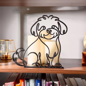 Matte black Maltipoo line art sculpture sitting on a wooden display shelf with warm candlelight behind it and colorful books below — modern 3D printed dog decor and a sweet Maltipoo gift for doodle dog moms, Maltipoo owners, and cute teddy-bear-style dog art fans.