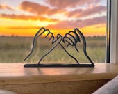 Minimalist pinky promise line art aculpture, displayed on a wooden shelf. This handmade line art decor features two hands linked in a pinky swear, symbolizing trust, loyalty, and love. Ideal as a friendship gift, romantic anniversary decoration, or stylish addition to modern and boho home decor. Surrounded by an amazing sunset with a golden sky, the sculpture creates a warm, aesthetic vibe.