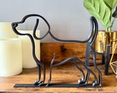 Minimalist beagle dog sculpture in matte black displayed on a wooden shelf with candles and plants. Modern single line art design makes it an ideal bookshelf accent or unique dog lover gift.