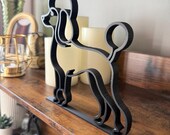 Side view of modern black poodle line art sculpture on a rustic shelf, styled with candles and gold decor accents.