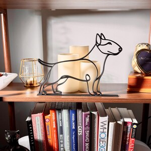 Bull terrier line art sculpture styled on a vintage wooden bookshelf with classic books, a warm amber candle, and decorative accents — minimalist 3D printed dog decor and a unique bull terrier gift idea for shelves, mantels, and modern dog lover homes.