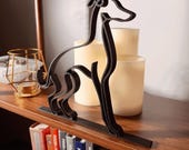 Angled view of a black Italian Greyhound line art statue on a wooden shelf with warm candlelight, highlighting the sleek minimalist silhouette and handcrafted 3D printed design.
