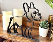 Modern French Bulldog decor sculpture shown in black matte finish on a rustic wooden shelf with candles in the background. Minimalist French Bulldog statue crafted in continuous single line art style, perfect for Frenchie enthusiasts and dog owners. Unique 3D printed shelf accent for office, living room, or bedroom spaces. Frenchie dog gift idea, durable yet lightweight, blends seamlessly with Scandinavian or modern design styles.