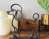 Minimalist black poodle line art sculpture in PLA plastic, standing on a wooden shelf with candles and a gold planter in the background.