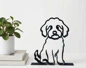 Minimalist Mini Goldendoodle sculpture next to a stack of books and a green potted plant in front of a white background.