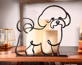 Matte black Bichon Frise line art sculpture sitting on a wooden display shelf with a glass lantern, warm candlelight, and a colorful bookshelf below — modern 3D printed dog decor and a sweet Bichon Frise gift for Bichon moms, white fluffy dog lovers, and small dog owners.