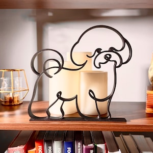 Matte black Bichon Frise line art sculpture sitting on a wooden display shelf with a glass lantern, warm candlelight, and a colorful bookshelf below — modern 3D printed dog decor and a sweet Bichon Frise gift for Bichon moms, white fluffy dog lovers, and small dog owners.