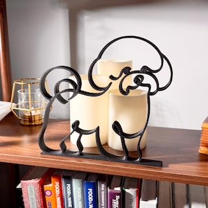 Sitting Bichon Frise line art sculpture with detailed cotton-ball fluffy coat displayed on a wooden shelf with warm glowing candles and a colorful bookshelf in the background — minimalist 3D printed Bichon Frise decor and a sweet Bichon Frise gift for dog moms, white fluffy dog lovers, and Bichon owners.