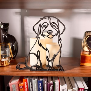 Sitting Bernedoodle line art sculpture with fluffy doodle coat displayed on a wooden shelf with warm glowing candles, a vintage clock, and a colorful bookshelf in the background — minimalist 3D printed Bernedoodle decor and a heartfelt Bernedoodle gift for dog moms, doodle owners, and Bernese poodle mix lovers.