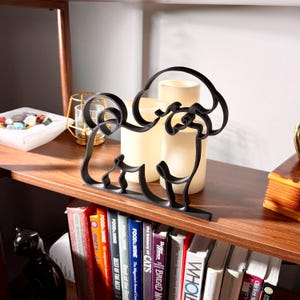 Close-up of a matte black Bichon Frise line art sculpture showing the breed's plush curly coat and cheerful expression, styled on a wooden shelf with vintage decor and bookshelf accents — 3D printed minimalist Bichon Frise decor and a thoughtful Bichon gift for dog moms and dog dads.