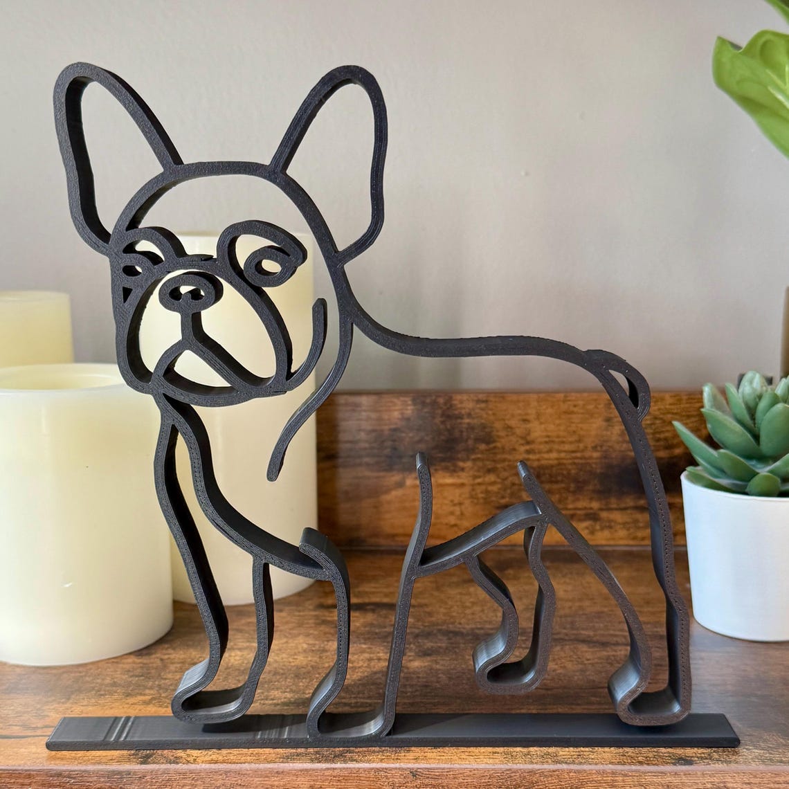 Front-facing French Bulldog sculpture in single-line art style. Matte black accent piece styled with candles and plants, perfect Frenchie gift or modern shelf decor.