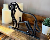 Side angle of Saint Bernard silhouette statue in matte black line art style, displayed with cozy shelf accents.