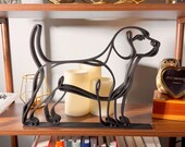 Hero shot of a large matte black Beagle line art sculpture in profile, backlit by warm pillar candles on a styled wooden shelf with a vintage clock, glassware, and cookbooks — oversized 3D printed beagle decor and a statement-size beagle gift for beagle owners and hound families.