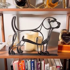 Hero shot of a large matte black Beagle line art sculpture in profile, backlit by warm pillar candles on a styled wooden shelf with a vintage clock, glassware, and cookbooks — oversized 3D printed beagle decor and a statement-size beagle gift for beagle owners and hound families.