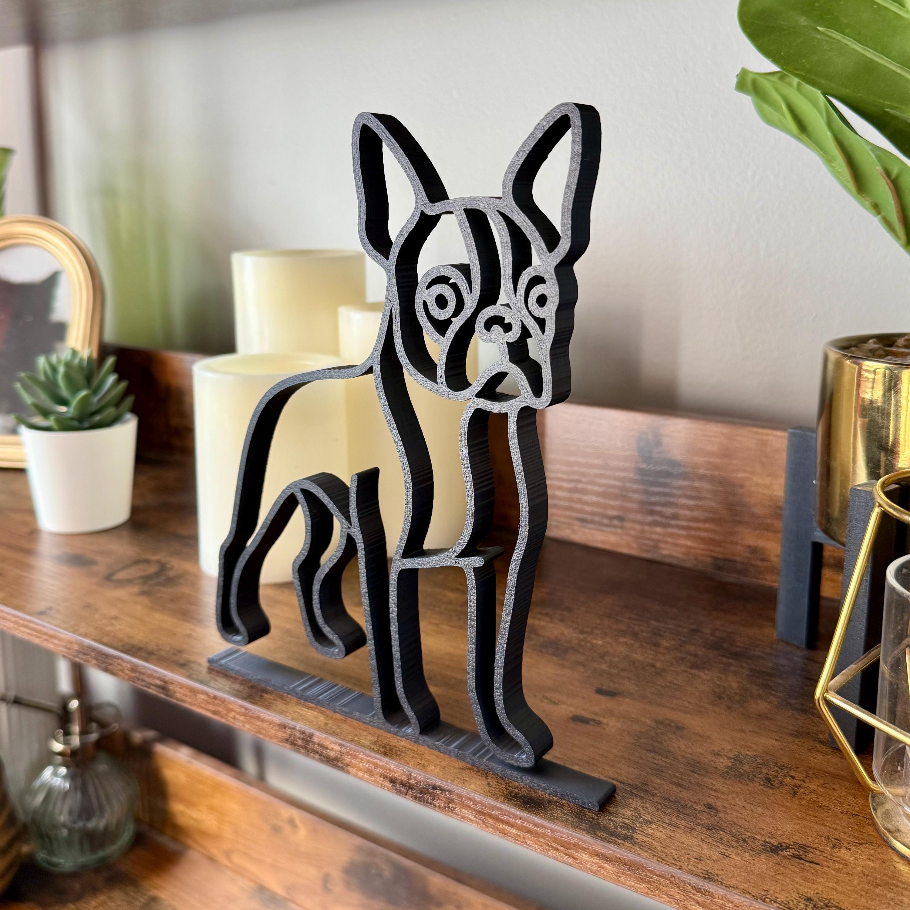 Matte black French Bulldog sculpture on small apartment desk next to laptop and plant