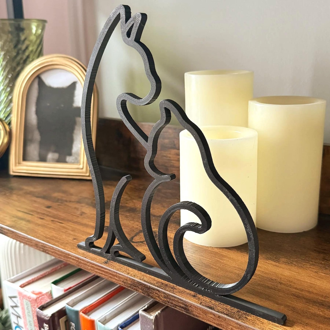 Minimalist black 3D printed cat line art sculpture featuring two cats sitting together, displayed on a rustic wood shelf with candles and books in the background. The sleek modern design adds a cozy, artistic touch to cat-themed home decor. Ideal for cat lovers, boho interiors, or as a thoughtful handmade gift.