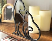 Minimalist black 3D printed cat line art sculpture featuring two cats sitting together, displayed on a rustic wood shelf with candles and books in the background. The sleek modern design adds a cozy, artistic touch to cat-themed home decor. Ideal for cat lovers, boho interiors, or as a thoughtful handmade gift.