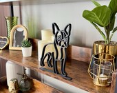 Minimalist Boston Terrier sculpture in matte black displayed on a wooden shelf with candles and greenery. Modern single line design makes it a perfect bookshelf accent or Boston Terrier lover gift.