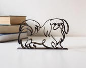 Minimalist black Pekingese silhouette statue beside stack of books on white desk, modern line drawing dog dad gift for Pekingese lover
