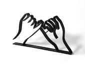 Minimalist black 3D printed pinky promise line art sculpture displayed on a clean white background. The design features two hands linking pinky fingers in a symbolic gesture of trust, loyalty, and love. Ideal as a friendship gift, romantic anniversary decor, or meaningful shelf art for modern and boho-style homes. This mockup showcases the sculpture’s sleek lines, clean base, and thoughtful handmade design, perfect for gifting or home styling.
