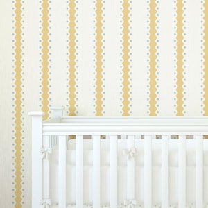May include: A white wooden crib featuring vertical slats and a solid frame. The crib is dressed with white bedding, including a skirt and a bumper adorned with small bows. The background consists of wallpaper with vertical yellow and white stripes.